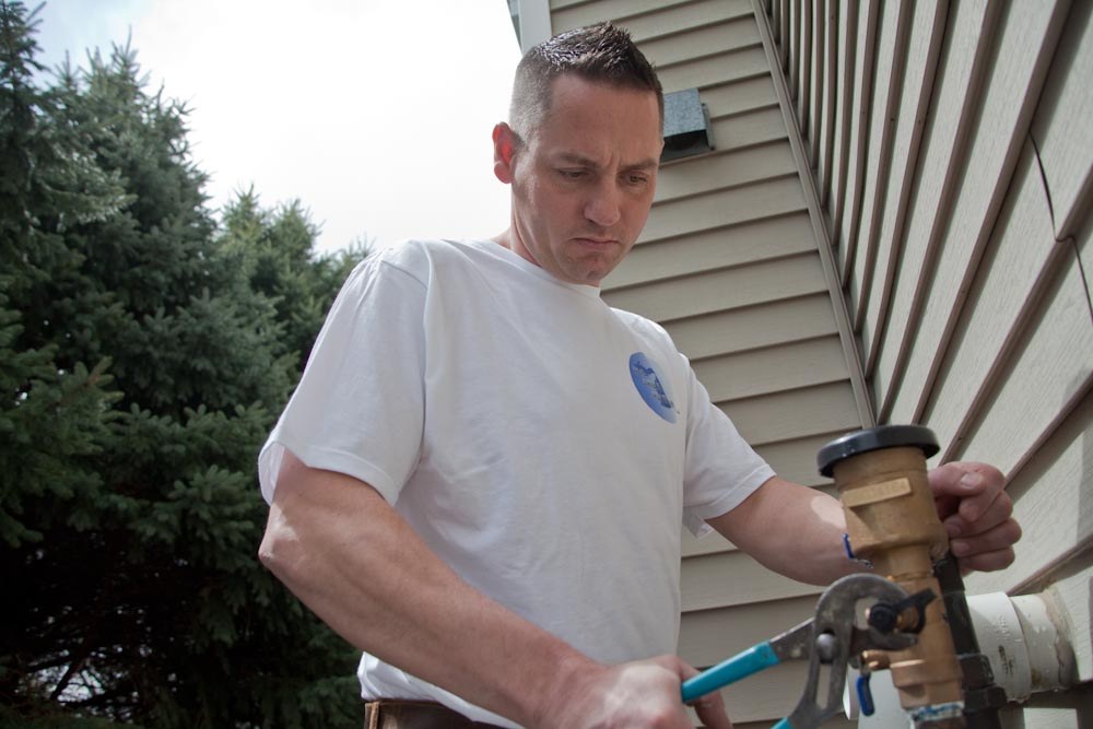 An All Area Plumbing owner repairing an outdoor pipe with a cutter
